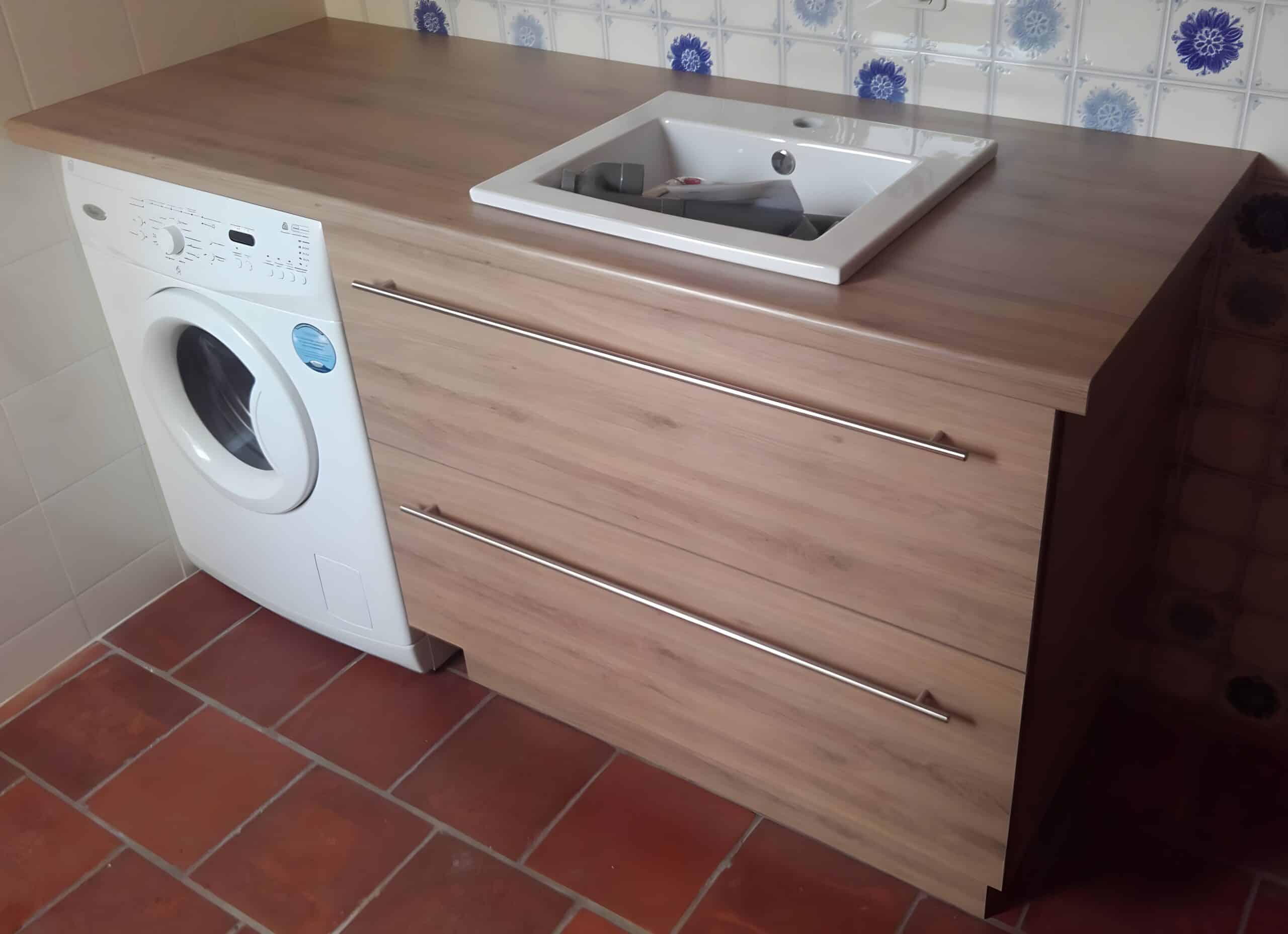 Buanderie lumineuse avec lave-linge Whirlpool blanc, évier encastré et meuble en bois clair. Mur carrelé motifs bleus, sol en terre cuite.