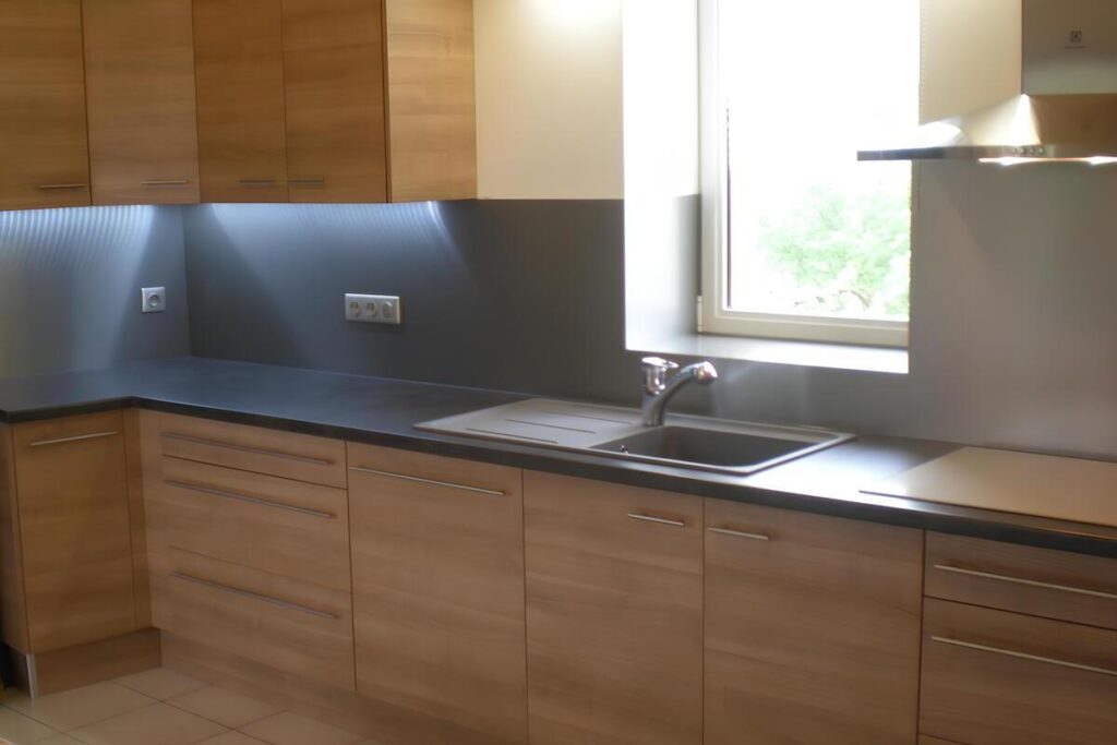 Cuisine moderne en bois clair et gris foncé avec évier inox, fenêtre lumineuse, hotte murale et prises électriques '330'.
