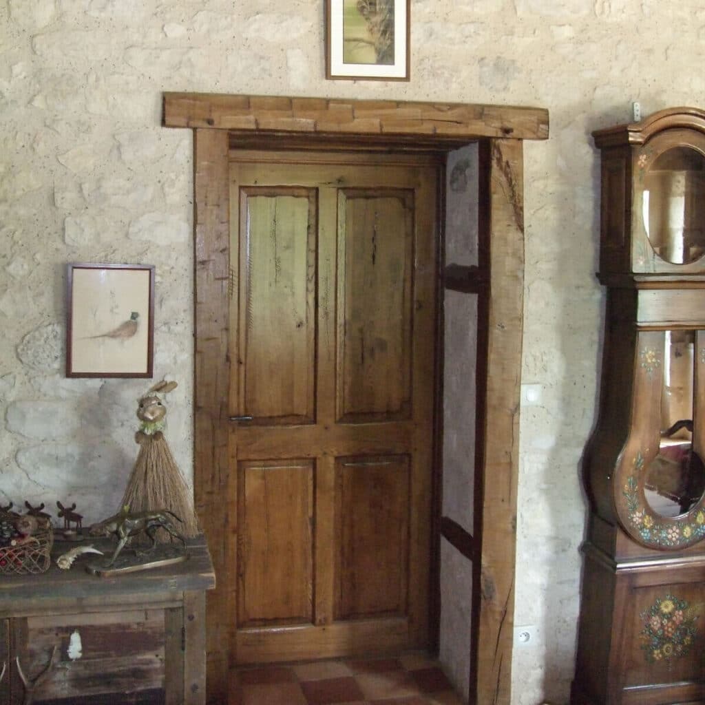 Porte en bois rustique avec encadrement épais dans un mur en pierre. Décoration avec horloge grand-père et cadre oiseau.